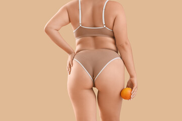 Wall Mural - Beautiful plus size woman in underwear with orange on beige background, back view. Cellulite concept