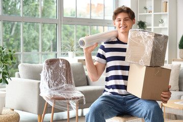 Sticker - Young man with roll of stretch film and cardboard boxes sitting in room on moving day