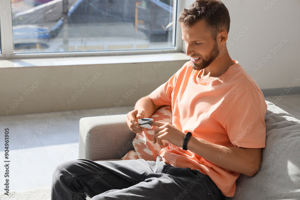 Young man with pulse oximeter sitting on sofa at home