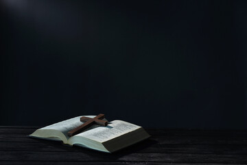 Wall Mural - Bible and cross on black wooden table against dark background, space for text. Religion of Christianity