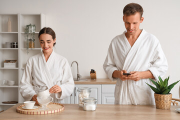 Sticker - Young man in bathrobe with mobile phone and his wife during breakfast at home