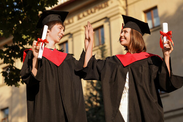 Poster - Graduating students with diplomas giving each other high-five outdoors