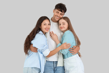 Poster - Young man with two women hugging on light background. Polyamory concept