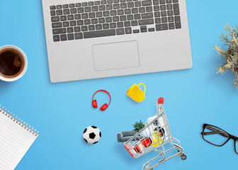Poster - Shopping cart on a desk with products around it and a laptop computer beside. Concept of online shopping and digital retail