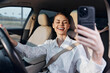 © SHOTPRIME STUDIO - A woman taking a selfie in her car, sitting in the driver's seat and holding her phone up to her face