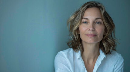 Wall Mural - 40-year-old women posing against a light background. Beautiful woman in a white shirt looks at the camera indoors. Beauty concept.