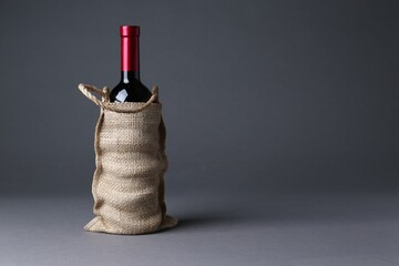 Sticker - Wine bottle in burlap bag on grey background, space for text