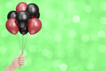 Aufkleber - child's hand holds bunch of red and black balloons on blurred summer green background. Empty space for text