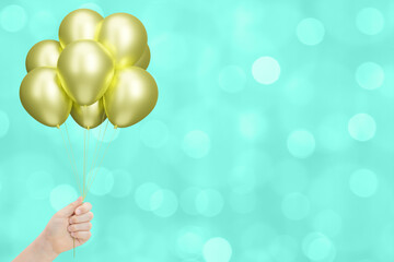 Aufkleber - Female hand holding bunch of shiny golden or yellow balloons on blurred aquamarine or green background. Empty space for text
