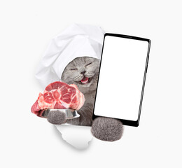 Poster - Happy cat wearing chef's hat looks through a hole in white paper, holds bowl with raw meat and shows smartphone with white blank screen in it paw, Empty free space for mock up, banner