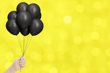Aufkleber - Female hand holds bunch of black balloons on blurred yellow or gold background. Empty space for text