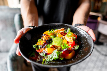 Sticker - A person holding a black plate with a vibrant salad featuring greens, tomatoes, and avocado. The colorful and fresh ingredients make it perfect for culinary and healthy eating themes. 