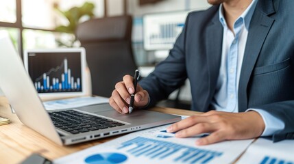 Poster - A business professional in a suit analyzes financial data on a laptop and paper reports in a bright, modern office filled with greenery and charts