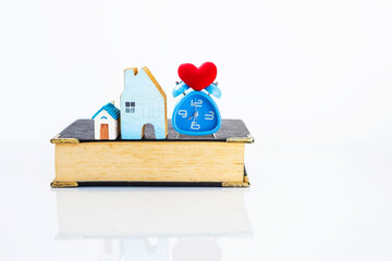 Wall Mural - Wooden house model and alarm clock with red heart on old book isolate on white background, home study and law, investment education concept