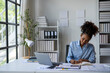 © Wasana - A woman is sitting at a desk with a laptop and a notebook