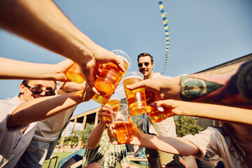 Wall Mural - Cheers to summer. Friends raise their glasses in a joyful toast at a sunny picnic. Positive vibes of outdoor catering. Concept of summer, leisure, friendship, meeting, fun and relaxation