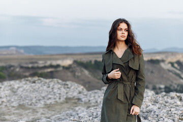 Wall Mural - Mysterious woman in trench coat standing on rocky hilltop overlooking scenic landscape