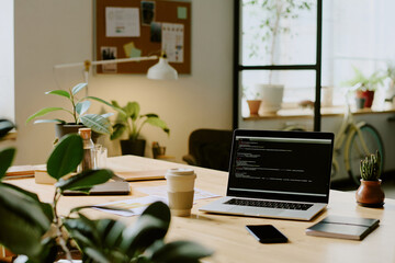 no people shot of laptop with code on screen, cup of coffee and smartphone on desk in modern eco-fri