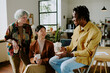 © AnnaStills - Three diverse gen Z male and female friends wearing stylish casual clothes enjoying coffee break at work in modern office
