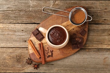 Sticker - Tasty melted chocolate in cup and spices on wooden table, top view