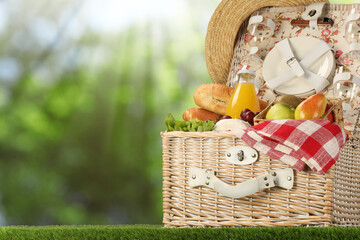 Canvas Print - Picnic basket with foods and juice on green grass outdoors. Space for text