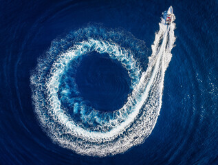 Wall Mural - aerial top view of a motor rib boat forming a circle of waves and bubbles with its engine over the b