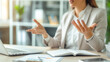 © Kiangdeb - Businesswoman gesturing during a discussion in an office setting, with a laptop and open book on the desk, indicating a professional meeting or presentation.