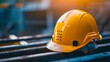 © Pornarun - A yellow hard hat sits on a metal beam, signifying construction or industrial work.  The sun shines brightly in the background, highlighting the hard hat's safety purpose.