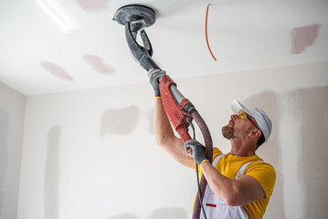 Wall Mural - The worker sanding a plasterboard ceiling. He is using special drywall sander. A red plasterboard improve the fire resistance of ceiling structures.