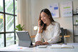 © PaeGAG - Young Professional Woman Smiling While Talking on Phone and Working on Tablet in Modern Office
