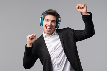 Brunette positive businessman listening music with headphones, grey studio