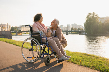 Wall Mural - Senior woman in wheelchair walking with caregiver old man on road. Elderly family couple man supporting taking care of paralyzed woman in chair for people with disability outdoor. Rehabilitation