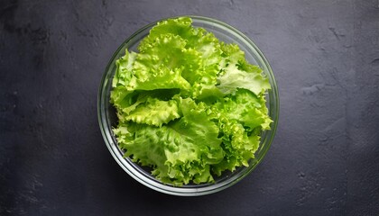 Wall Mural - top view of fresh green lettuce leaves in a glass bowl on a dark background healthy eating and vegetarian food concept