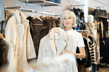 Mature lady carefully inspects fur coats, contemplating which one best complements her winter wardrobe.