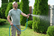 © New Africa - Man watering lawn with hose in backyard