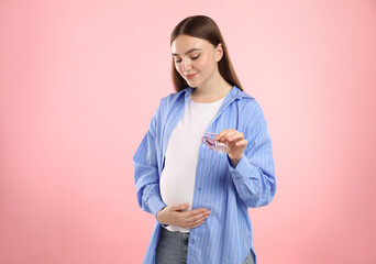 Sticker - Expecting twins. Pregnant woman holding two pacifiers on pink background