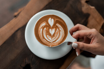 Cup of coffee in hand. Latte art in white mug. 