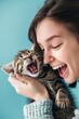 © tantawat - Delighted Woman Playing with Kitten on Light Blue Background, Copyspace for Pet Message.