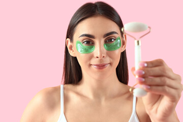 Sticker - Pretty young woman with under-eye patches and face massage roller on pink background