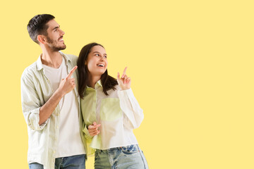 Poster - Happy young couple pointing at something on yellow background