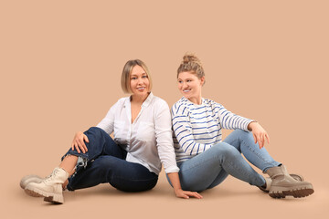 Wall Mural - Beautiful happy women in stylish jeans sitting on beige background