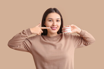 Poster - Young Asian woman pointing at jaw model on beige background