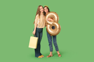 Wall Mural - Happy young sisters holding balloon in shape of figure 8 with shopping bag on green background