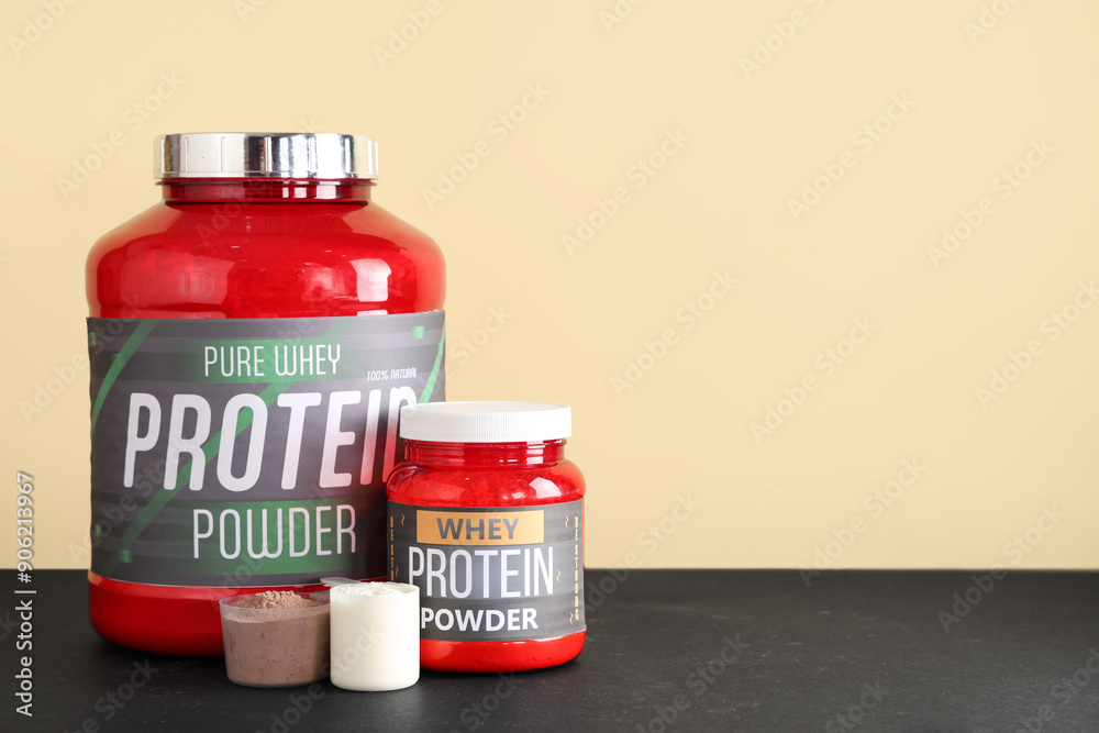 Bottles and scoops with protein powder on dark table against color background