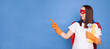 © sementsova321 - Astonished shocked woman posing as superhero with mask and cape holding detergent spray and brush performing household tasks isolated over blue background pointing at advertisement area