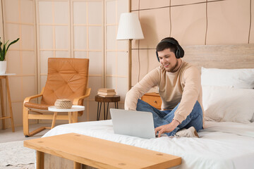 Sticker - Young bearded man with headphones using laptop in bedroom