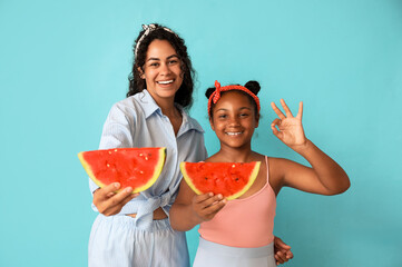 Canvas Print - Beautiful young African-American woman and her cute daughter with slices of fresh watermelon showing ok gesture on blue background