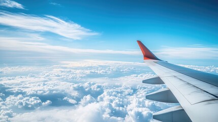 Wall Mural - Airplane wing close-up over a clear blue sky with decorative cumulus clouds, capturing a panoramic view perfect for travel promotions.