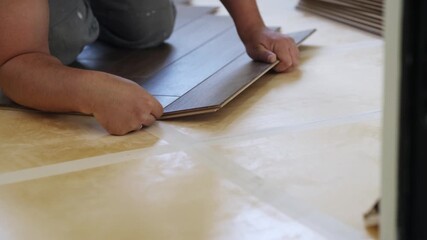 Poster - Close-up of a man kneeling and installing laminate flooring in a home. Focus on hands carefully placing panels. Perfect for DIY, renovation, and interior design projects
