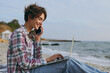 © ViDi Studio - Young IT woman wear shirt casual clothes work hold use laptop pc computer speak on mobile cell phone sits rest on sea ocean sand shore beach outdoor seaside in summer day free time. Lifestyle concept.